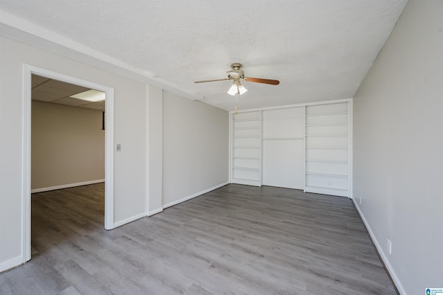 unfurnished bedroom featuring a closet, a textured ceiling, baseboards, and wood finished floors