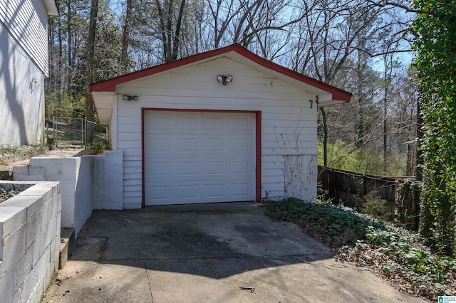 detached garage featuring concrete driveway and fence