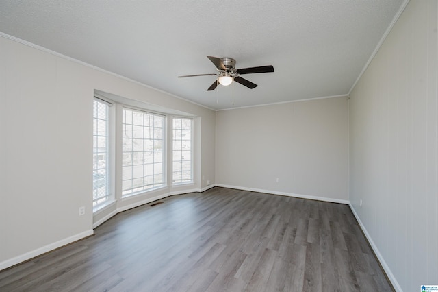 empty room with visible vents, wood finished floors, baseboards, and ornamental molding