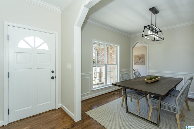 dining space with crown molding, a chandelier, dark wood finished floors, wainscoting, and arched walkways