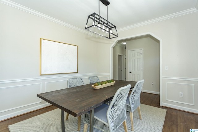 dining room featuring crown molding, a decorative wall, dark wood-style floors, and arched walkways