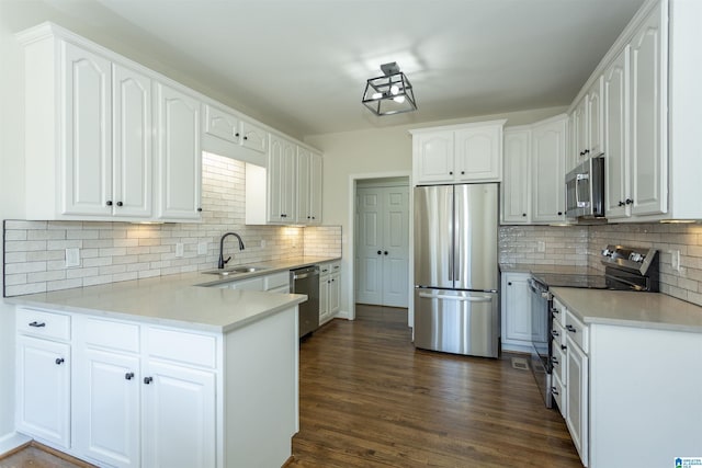 kitchen featuring dark wood-type flooring, appliances with stainless steel finishes, a peninsula, white cabinets, and a sink