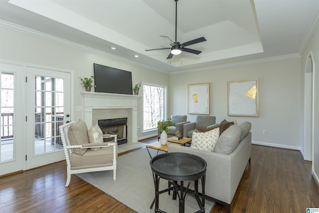 living room with a ceiling fan, dark wood finished floors, a fireplace with flush hearth, crown molding, and a raised ceiling