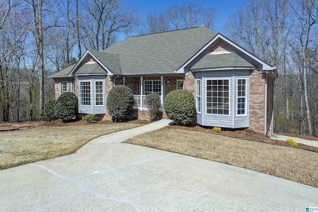 view of front of home with brick siding, covered porch, and roof with shingles