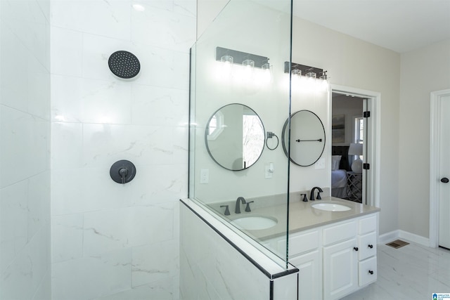 ensuite bathroom with double vanity, marble finish floor, tiled shower, and a sink