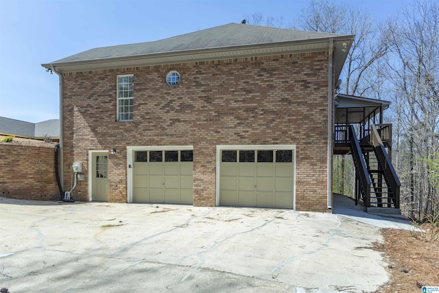 view of home's exterior with stairs, an attached garage, brick siding, and driveway