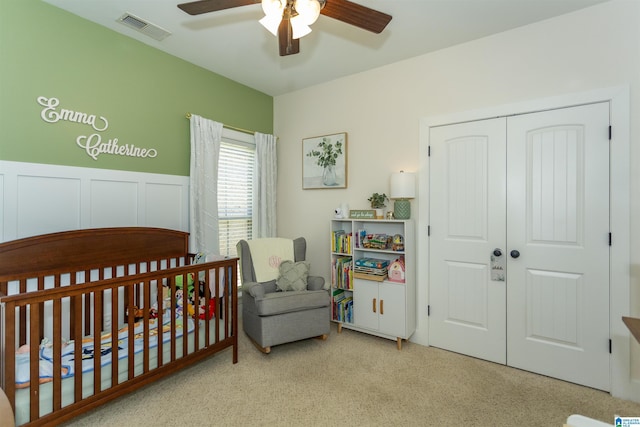 bedroom featuring visible vents, a wainscoted wall, a closet, a nursery area, and ceiling fan