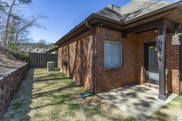 view of property exterior with central air condition unit, brick siding, a yard, and fence