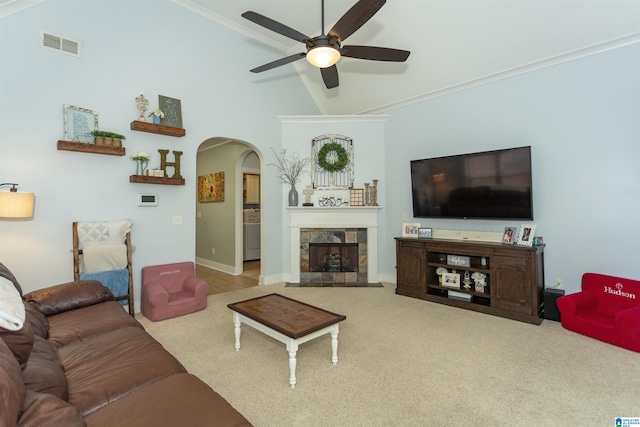 carpeted living area featuring visible vents, a ceiling fan, a tiled fireplace, arched walkways, and vaulted ceiling