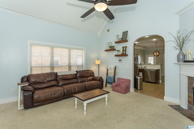 carpeted living area with high vaulted ceiling, ornamental molding, arched walkways, a fireplace, and ceiling fan