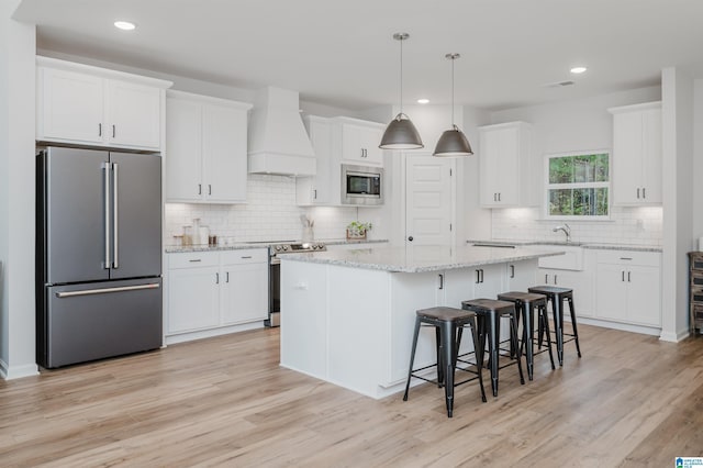 kitchen with white cabinets, appliances with stainless steel finishes, a center island, and custom range hood