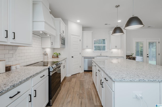 kitchen with visible vents, stainless steel appliances, custom range hood, white cabinetry, and a center island