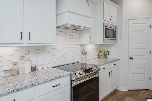 kitchen with light stone counters, wood finished floors, premium range hood, stainless steel appliances, and white cabinetry