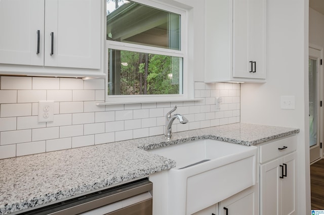 kitchen with a sink, backsplash, stainless steel dishwasher, white cabinetry, and light stone countertops