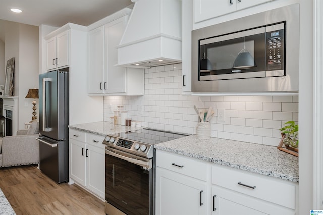 kitchen with light stone countertops, light wood finished floors, custom exhaust hood, stainless steel appliances, and white cabinetry