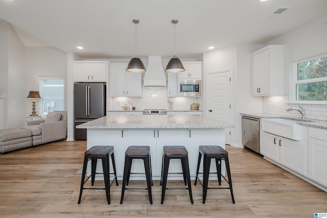 kitchen featuring light wood finished floors, a center island, a kitchen bar, stainless steel appliances, and white cabinetry