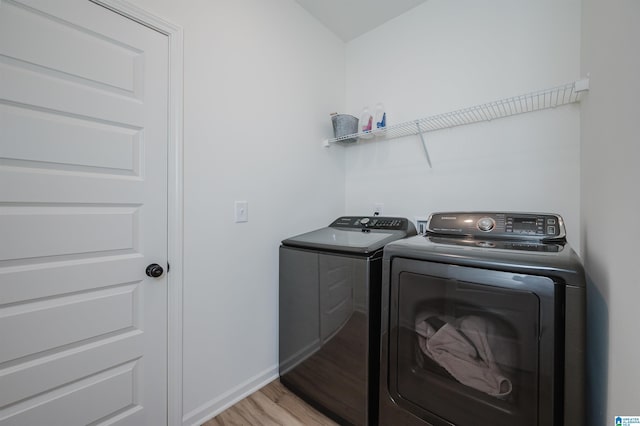 clothes washing area with washer and dryer, baseboards, light wood-style floors, and laundry area