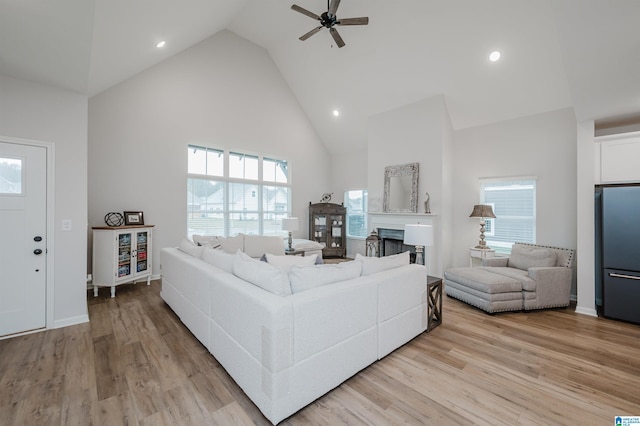 living room featuring a ceiling fan, a fireplace, light wood-type flooring, and high vaulted ceiling