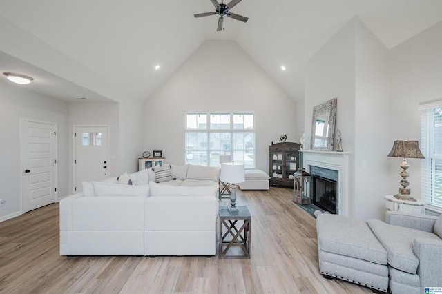 living area with high vaulted ceiling, ceiling fan, a high end fireplace, and light wood finished floors