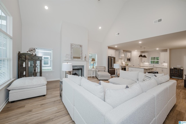 living room with visible vents, baseboards, high vaulted ceiling, a fireplace, and light wood-style floors