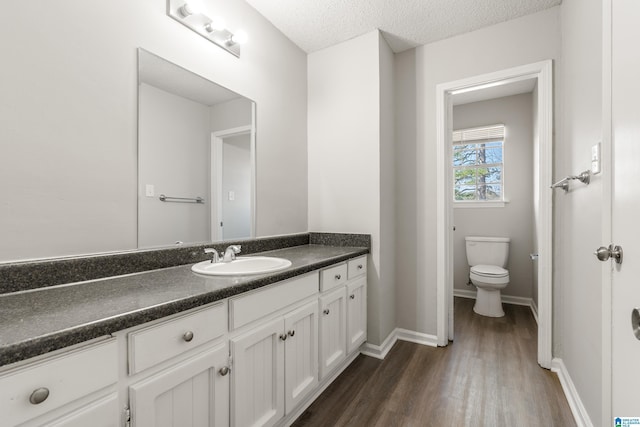 bathroom with baseboards, toilet, vanity, wood finished floors, and a textured ceiling