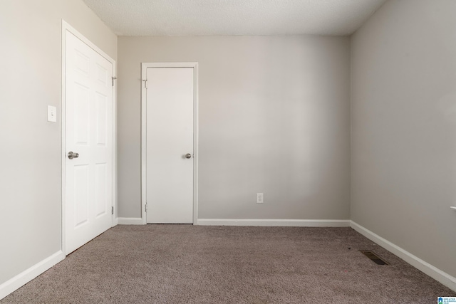 empty room with carpet flooring, baseboards, visible vents, and a textured ceiling