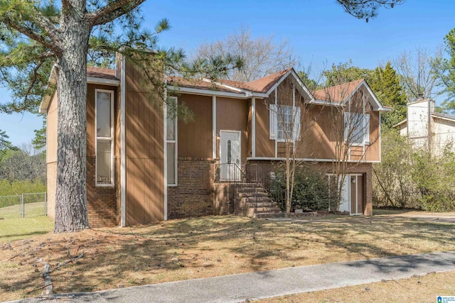 raised ranch with brick siding, a front lawn, and fence