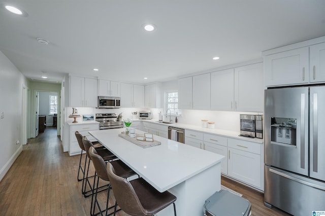 kitchen featuring dark wood-style floors, a sink, stainless steel appliances, a kitchen breakfast bar, and a center island