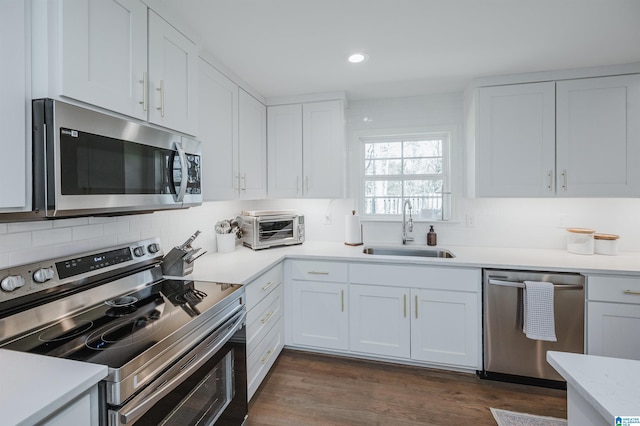 kitchen with a sink, dark wood-style floors, appliances with stainless steel finishes, white cabinets, and light countertops