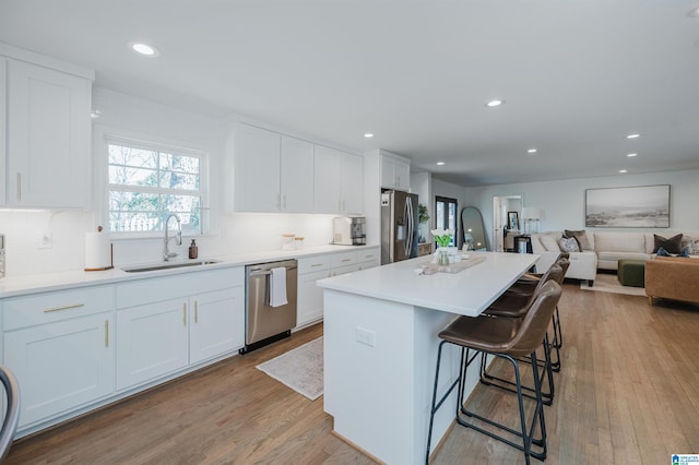 kitchen with white cabinetry, stainless steel appliances, light wood-style floors, and a sink