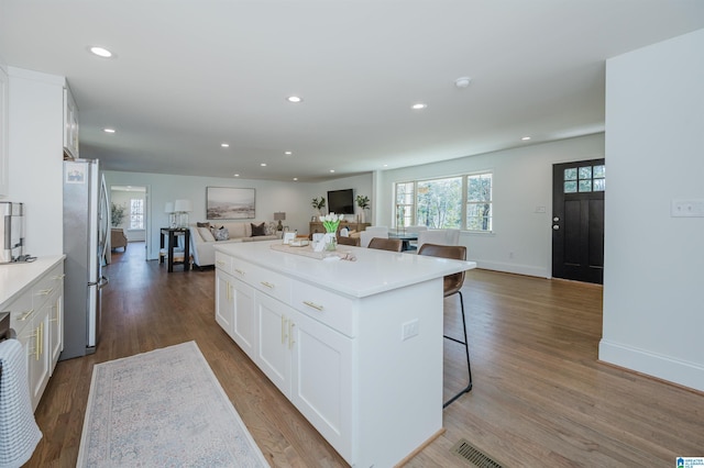 kitchen with a kitchen island, open floor plan, a kitchen bar, freestanding refrigerator, and white cabinetry