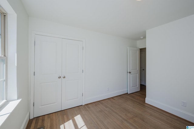 unfurnished bedroom with wood finished floors, baseboards, and a closet