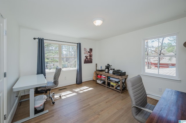 office space featuring plenty of natural light, visible vents, baseboards, and light wood-style floors