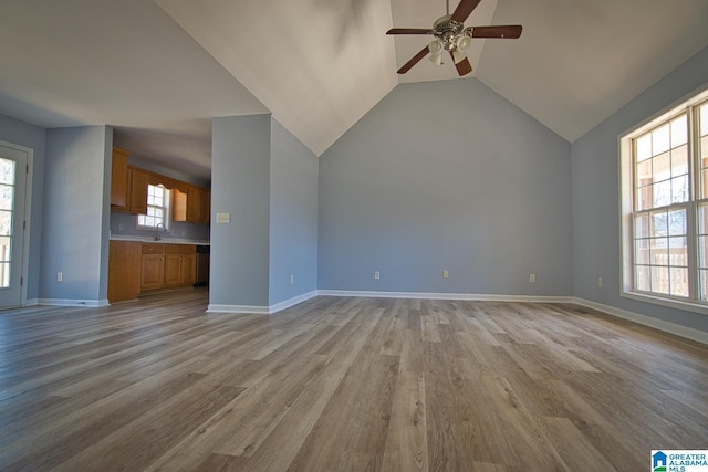 unfurnished living room with light wood finished floors, baseboards, lofted ceiling, a ceiling fan, and a sink