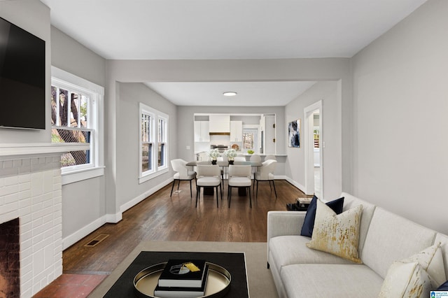 living room featuring visible vents, a fireplace, baseboards, and wood finished floors