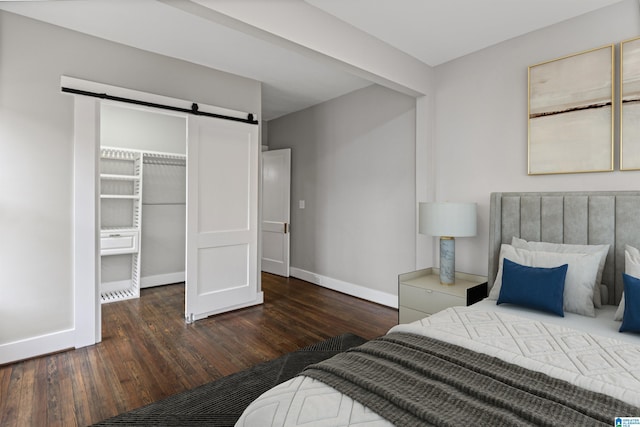 bedroom with a barn door, dark wood-style floors, baseboards, and a closet