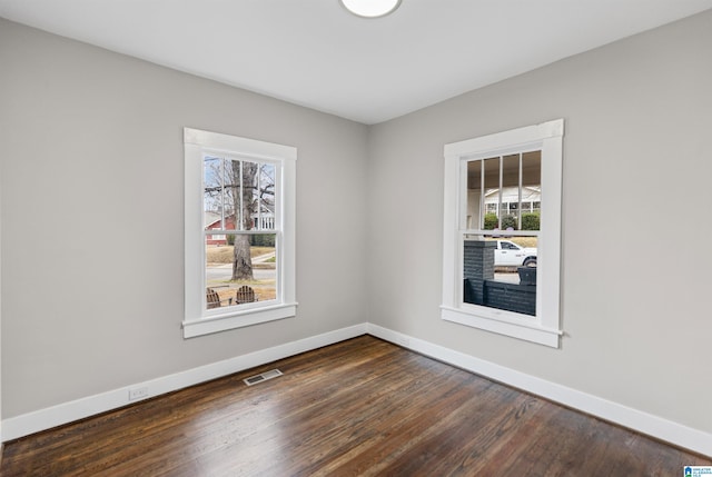 spare room featuring dark wood-type flooring, visible vents, and baseboards