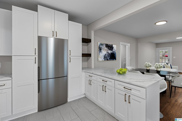 kitchen featuring a peninsula, white cabinetry, and freestanding refrigerator