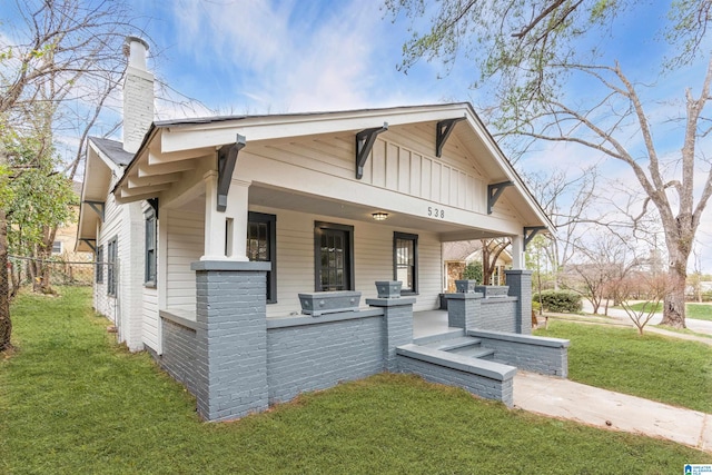 view of front facade featuring a porch, a chimney, a front lawn, board and batten siding, and brick siding