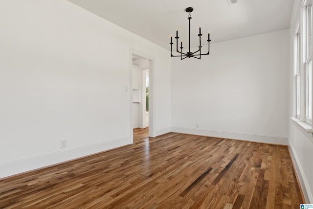 unfurnished room featuring a chandelier, baseboards, and wood finished floors