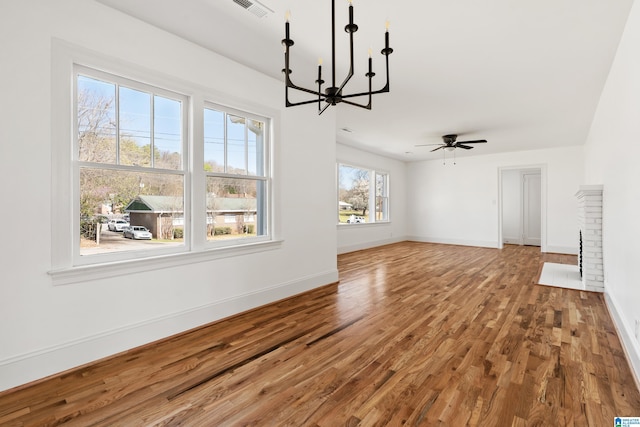 unfurnished living room with ceiling fan with notable chandelier, a fireplace, baseboards, and wood finished floors