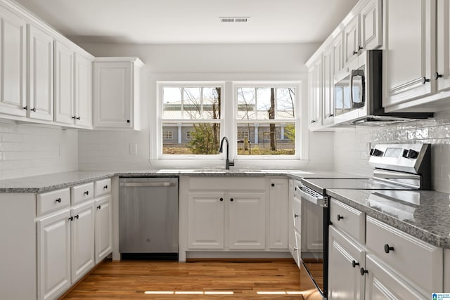 kitchen featuring visible vents, a sink, stainless steel appliances, light wood-style floors, and white cabinets