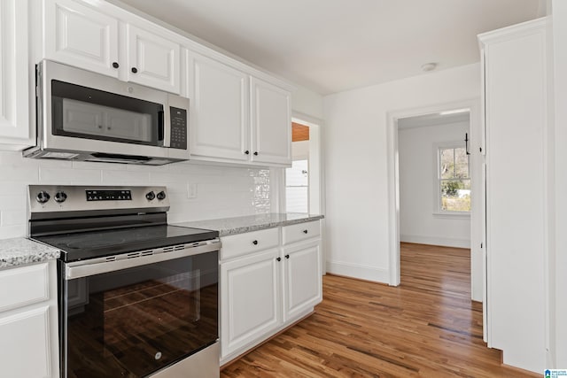 kitchen with light wood-type flooring, stainless steel appliances, white cabinets, and decorative backsplash