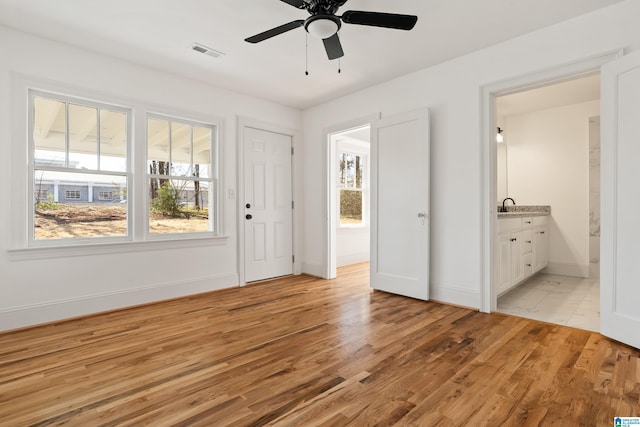 unfurnished bedroom featuring light wood-type flooring, visible vents, ensuite bathroom, a sink, and baseboards