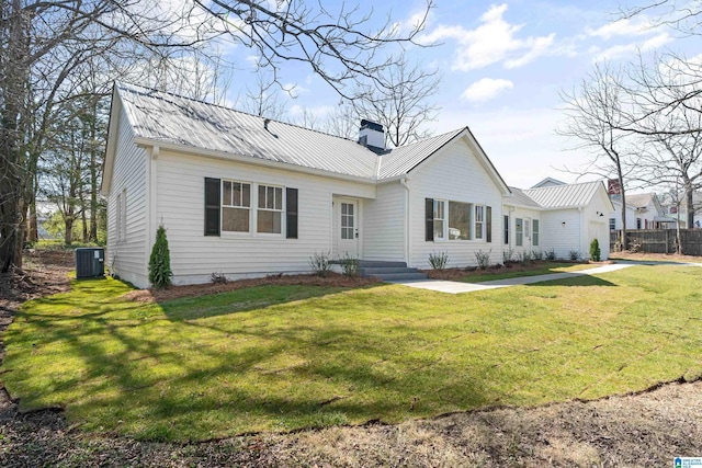 rear view of house featuring fence, central AC, a lawn, a chimney, and metal roof