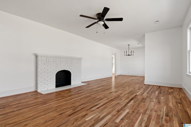 unfurnished living room with visible vents, ceiling fan with notable chandelier, wood finished floors, a fireplace, and baseboards