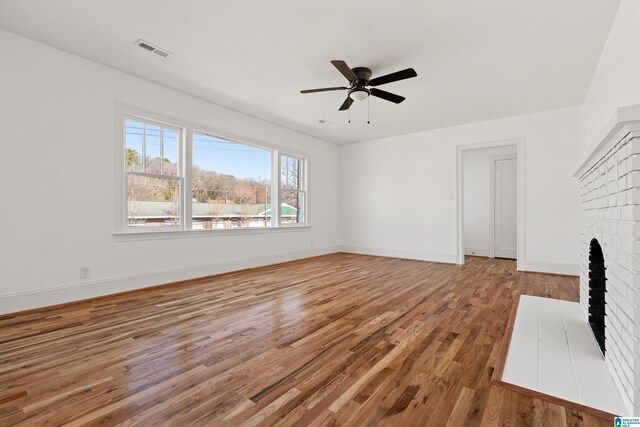 unfurnished living room featuring visible vents, a brick fireplace, baseboards, wood finished floors, and a ceiling fan