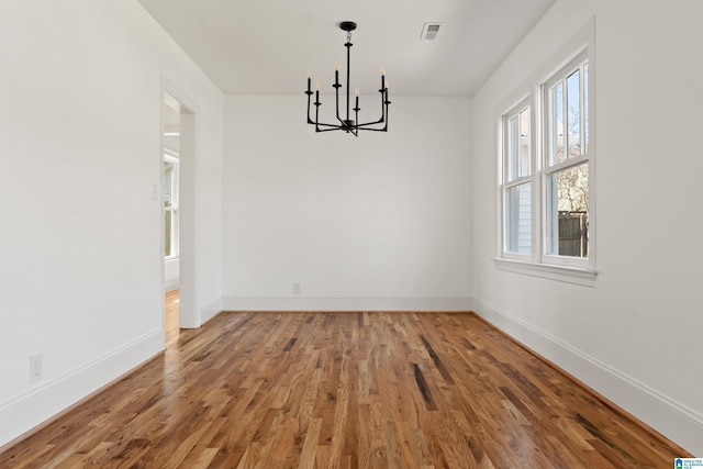 unfurnished dining area with an inviting chandelier, wood finished floors, visible vents, and baseboards