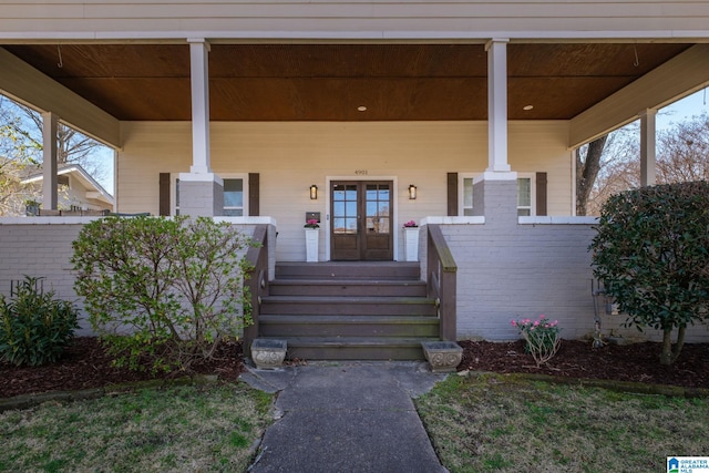 view of exterior entry with french doors, brick siding, and a porch