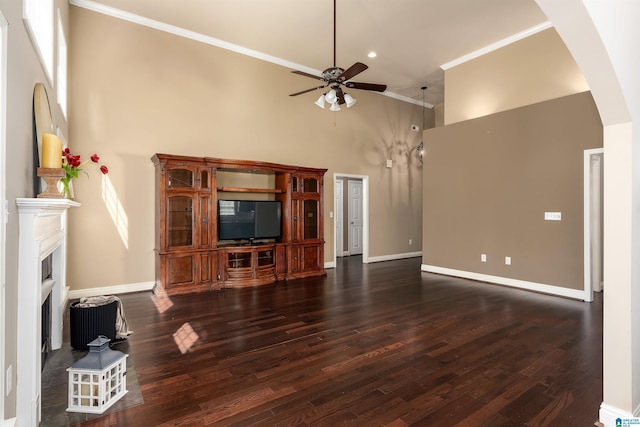 unfurnished living room featuring wood finished floors, arched walkways, a fireplace with raised hearth, and crown molding